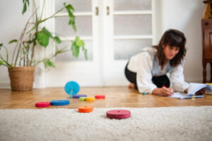 Mutter sitzt zwischen Spielzeug am Boden und schreibt achtsam – Selbstfürsorge im Familienalltag